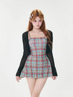 Full body shot of a woman wearing a plaid mini dress and a sheer black cardigan.