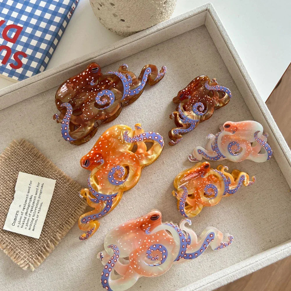 A top-down view of a tray filled with octopus-shaped hair clips in translucent orange, brown, and pinkish-white hues, accented with white dots and blue tentacles.