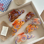 A top-down view of a tray filled with octopus-shaped hair clips in translucent orange, brown, and pinkish-white hues, accented with white dots and blue tentacles.