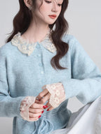 Close-up of a woman's chest and hands wearing a light blue knit cardigan with a white lace collar and cuffs.