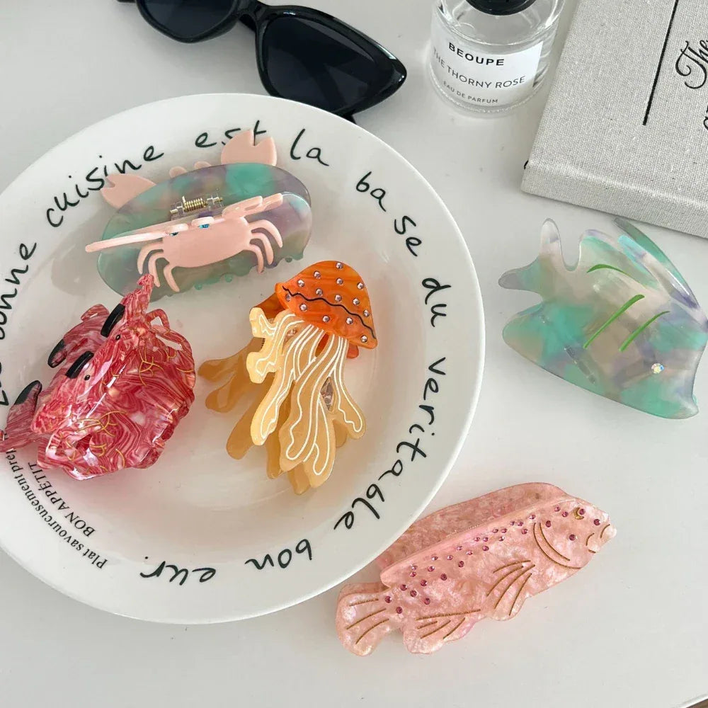 Close-up of ocean-themed hair clips on a white surface, featuring a jellyfish, crab, and fish