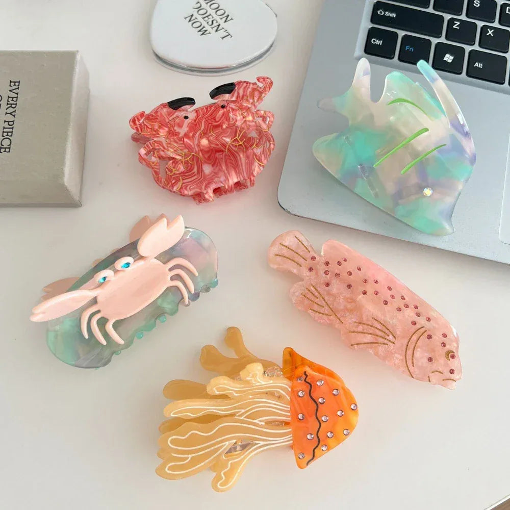 Various ocean-themed hair clips, including a jellyfish, crab, and fish, placed on a white desk near a laptop