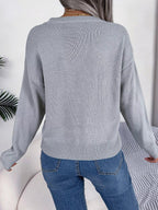 Back view of a woman wearing a grey knit sweater with blue jeans.