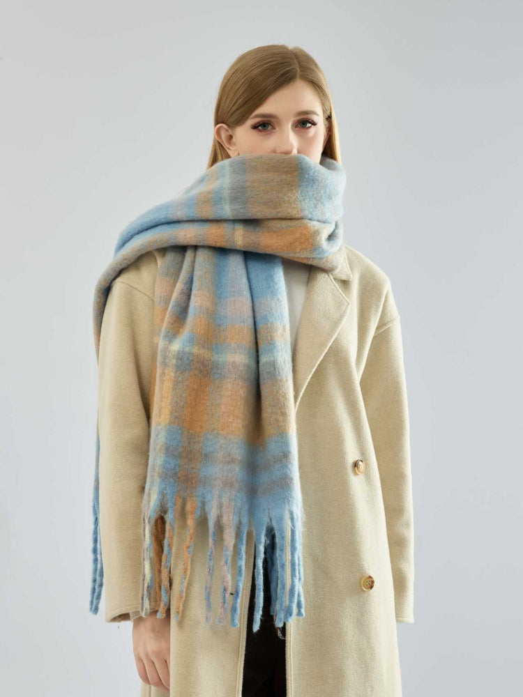 Woman wearing a beige coat and a blue and tan plaid scarf wrapped around her neck.