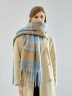 Woman wearing a beige coat and a blue and tan plaid scarf wrapped around her neck.
