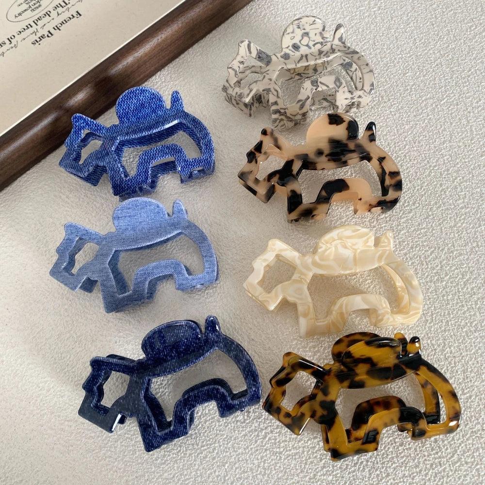 A top-down view of several elephant-shaped hair claw clips in different colors and patterns, displayed on a white textured surface.