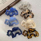 A top-down view of several elephant-shaped hair claw clips in different colors and patterns, displayed on a white textured surface.
