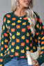 Close-up on the front of a dark green sweater featuring a repeating pattern of orange and yellow maple leaves. The knit texture is visible.