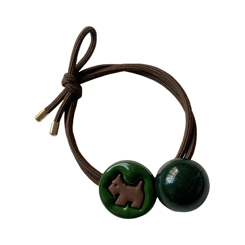Brown elastic hair tie with a green circular charm featuring a brown dog silhouette and a dark green round bead. Main image
