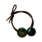Brown elastic hair tie with a green circular charm featuring a brown dog silhouette and a dark green round bead.