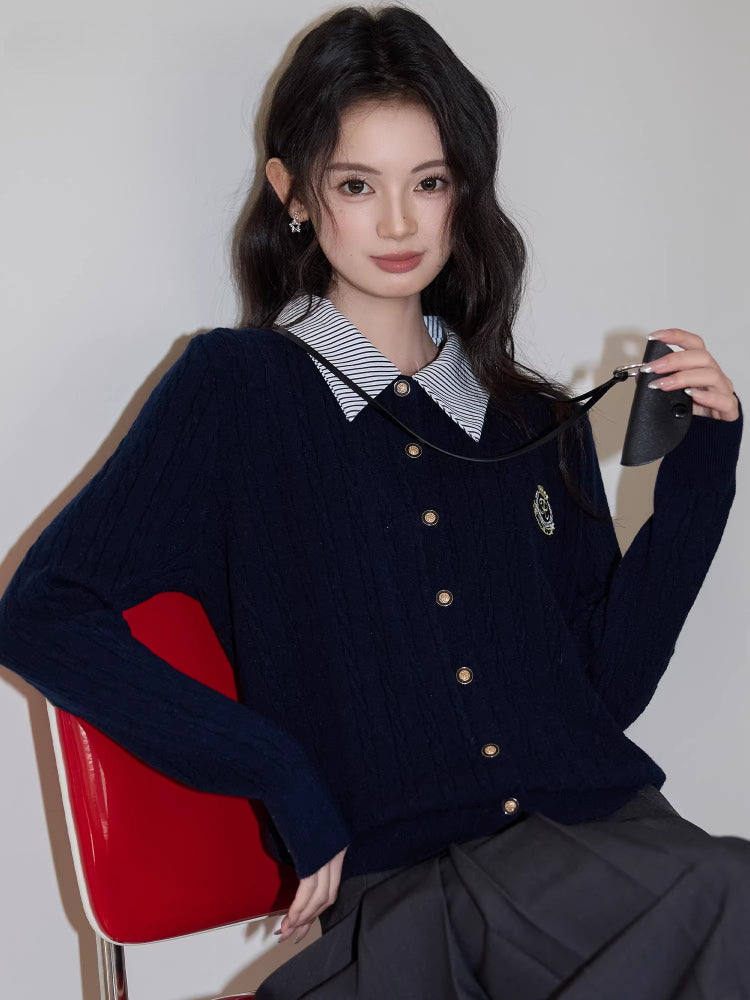 Close-up of a woman wearing a navy blue cable knit cardigan with a striped collar and a gray pleated skirt.