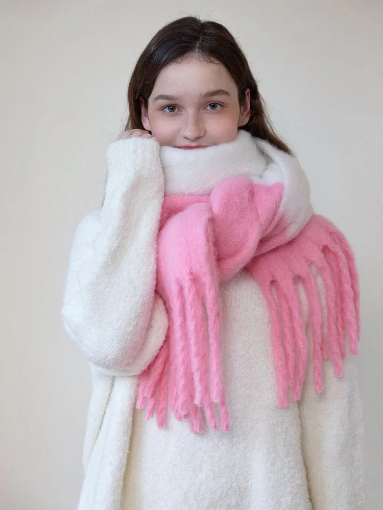 Close-up of a woman wearing a white sweater and a white and pink two-tone fuzzy knit scarf with fringe trim, adjusting the scarf.