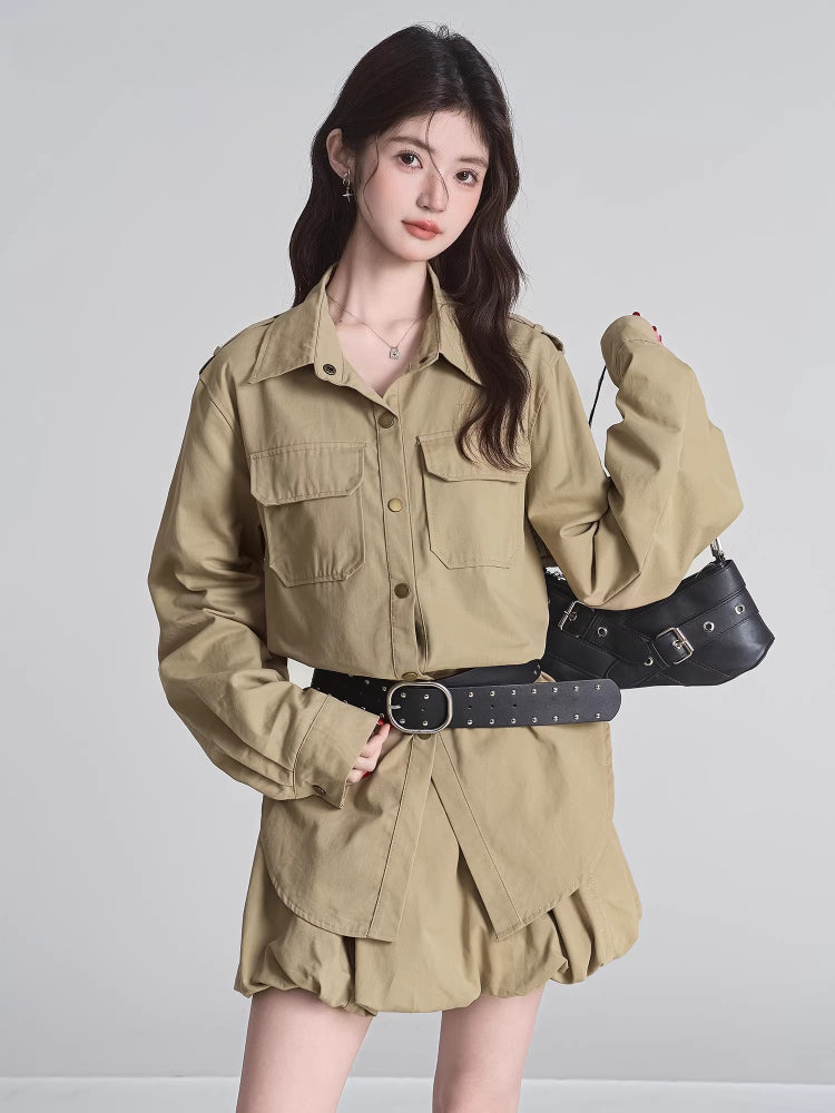Model holding a black handbag while wearing a tan shirt dress with a gathered skirt and black belt.