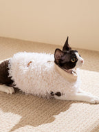 Black and white cat resting on a carpet wearing a white sherpa fleece vest.