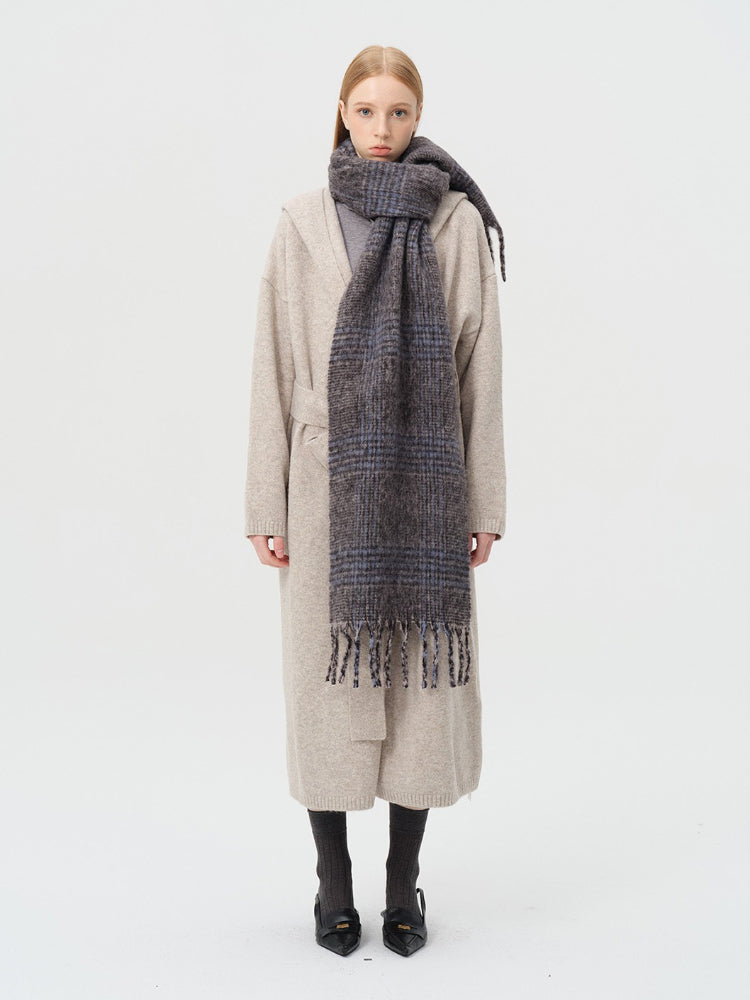 Model wearing a long, plaid scarf with fringe details over a beige cardigan.