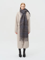 Model wearing a long, plaid scarf with fringe details over a beige cardigan.