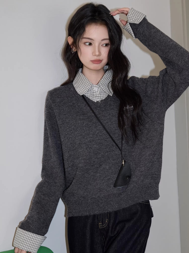 Woman standing with her hand on her head, wearing a grey v-neck sweater over a checkered collared shirt, dark wash wide leg jeans, and a black crossbody pouch.