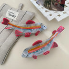 Two clear resin fish hair clips with pink fins and rainbow stripes displayed on a textured fabric.