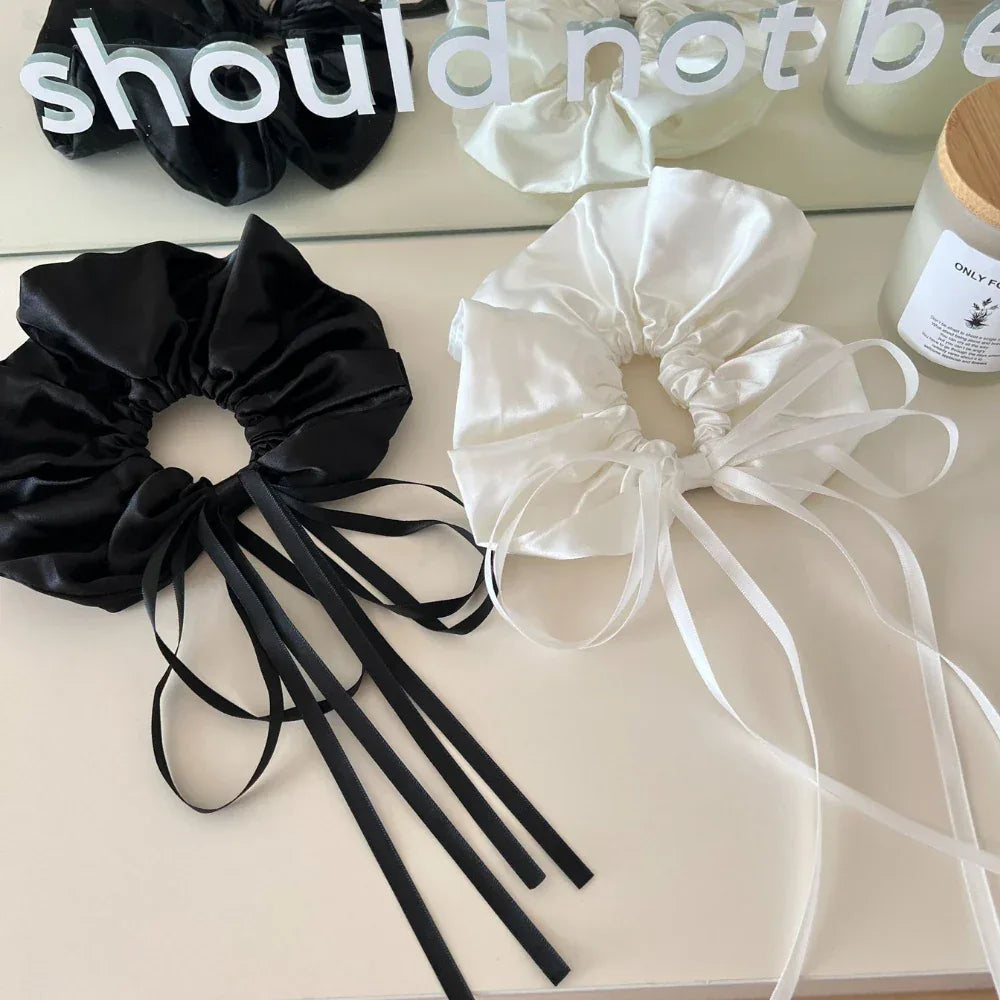 black and white satin scrunchies with long ribbon ties on a white surface