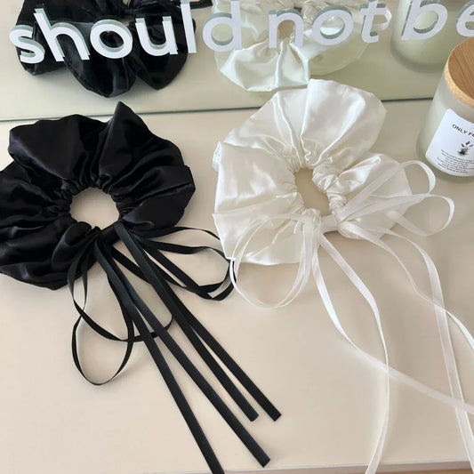 black and white satin scrunchies with long ribbon ties on a white surface