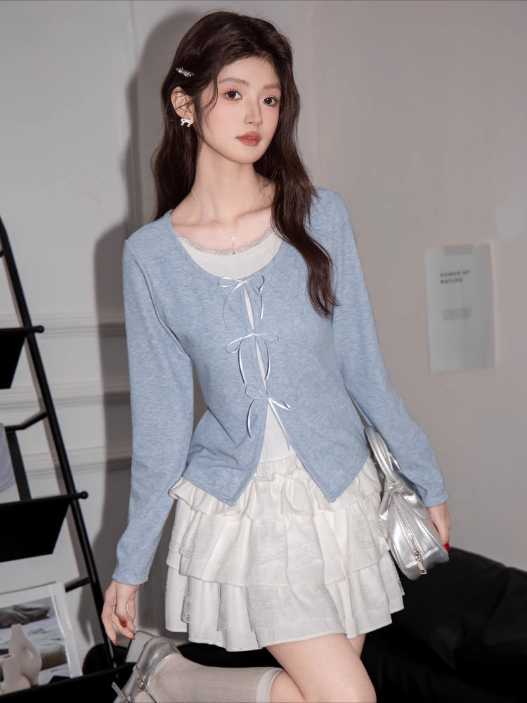 A young woman poses in a light blue cardigan and white ruffled skirt, holding a silver handbag.