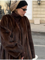 Close-up of a woman wearing a brown mink fur coat and a black turtleneck, with sunglasses and a black headband.