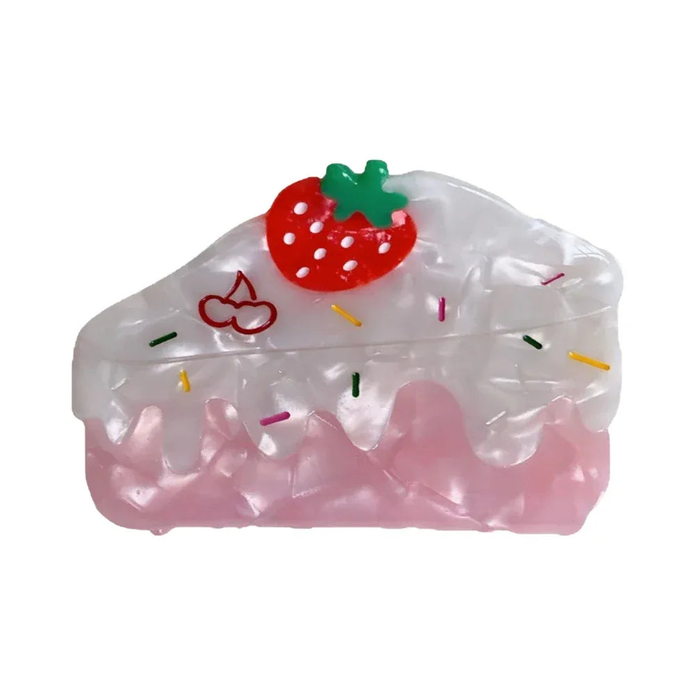 A close-up shot of a single strawberry cake-shaped hair claw clip, featuring a red strawberry with a green stem on top, white frosting with colorful sprinkles, and a pink base. Main image