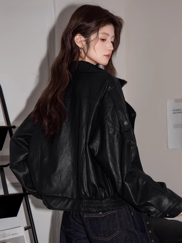 Back view of a woman wearing a black faux leather jacket with elasticated hem and zippered cuffs.