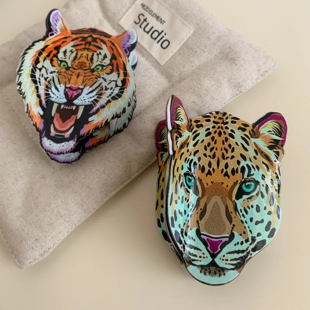 A tiger head accessory and a leopard head accessory displayed on a textured fabric background