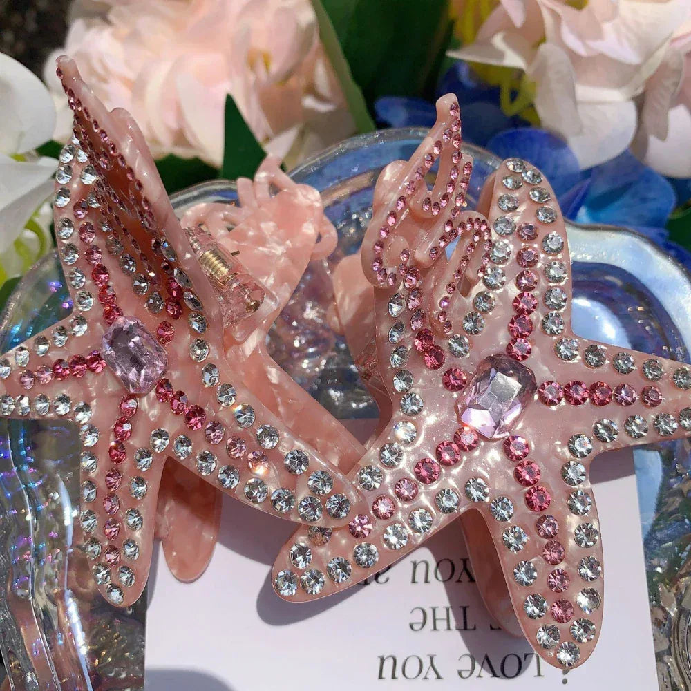 Two pink rhinestone-embellished starfish hair claw clips on a decorative plate
