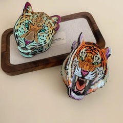 A tiger head accessory and a leopard head accessory resting on a wooden tray with a fabric insert