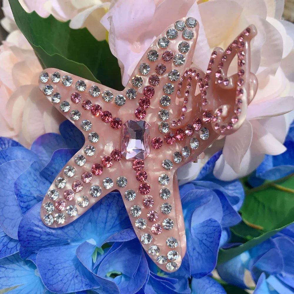 A pink rhinestone-embellished starfish hair claw clip resting on blue and pink flowers