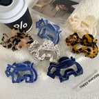 Several elephant-shaped hair claw clips are scattered on a white towel next to a coffee cup and a magazine.