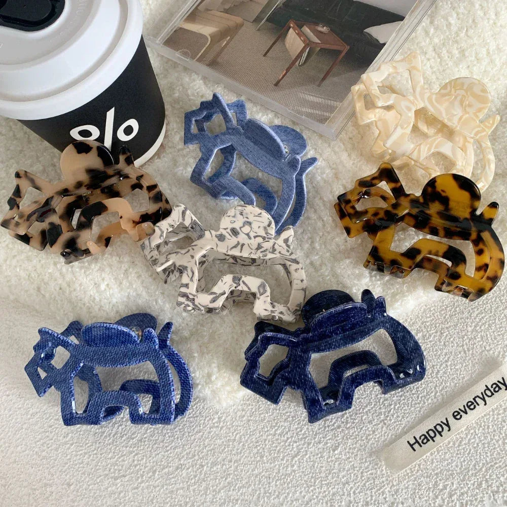Several elephant-shaped hair claw clips are scattered on a white towel next to a coffee cup and a magazine.