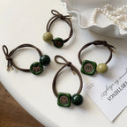 Four hair ties displayed on a white surface, each with different charms and bead combinations.