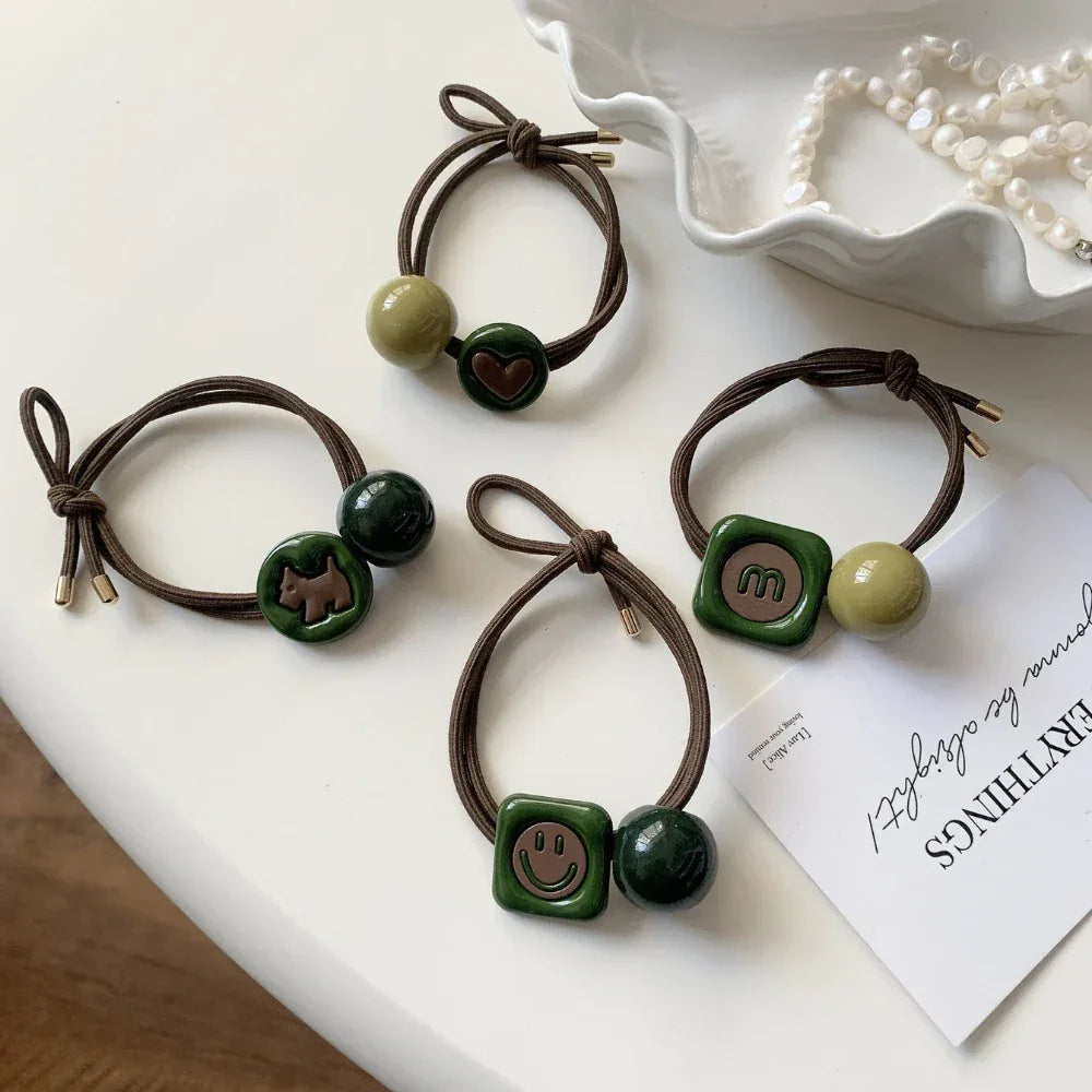 Four hair ties displayed on a white surface, each with different charms and bead combinations.