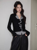 Full body shot of a woman in a black and grey top with ruffled detail and dark jeans.