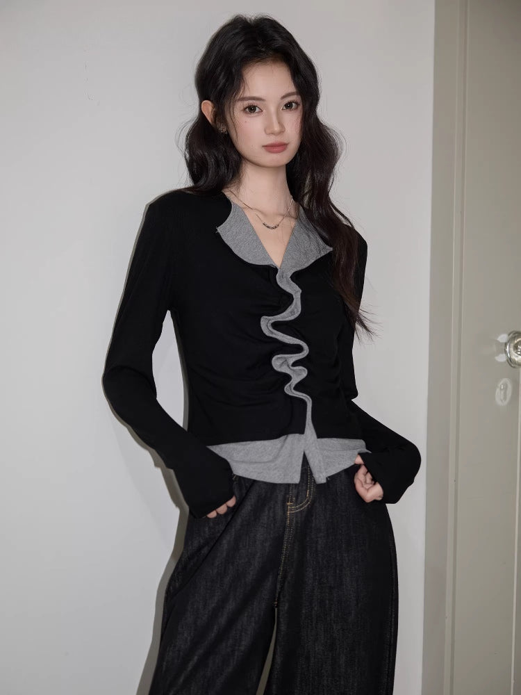 Full body shot of a woman in a black and grey top with ruffled detail and dark jeans.