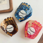 Top-down view of three marbled acrylic baseball glove hair claw clips in blue, brown, and pink