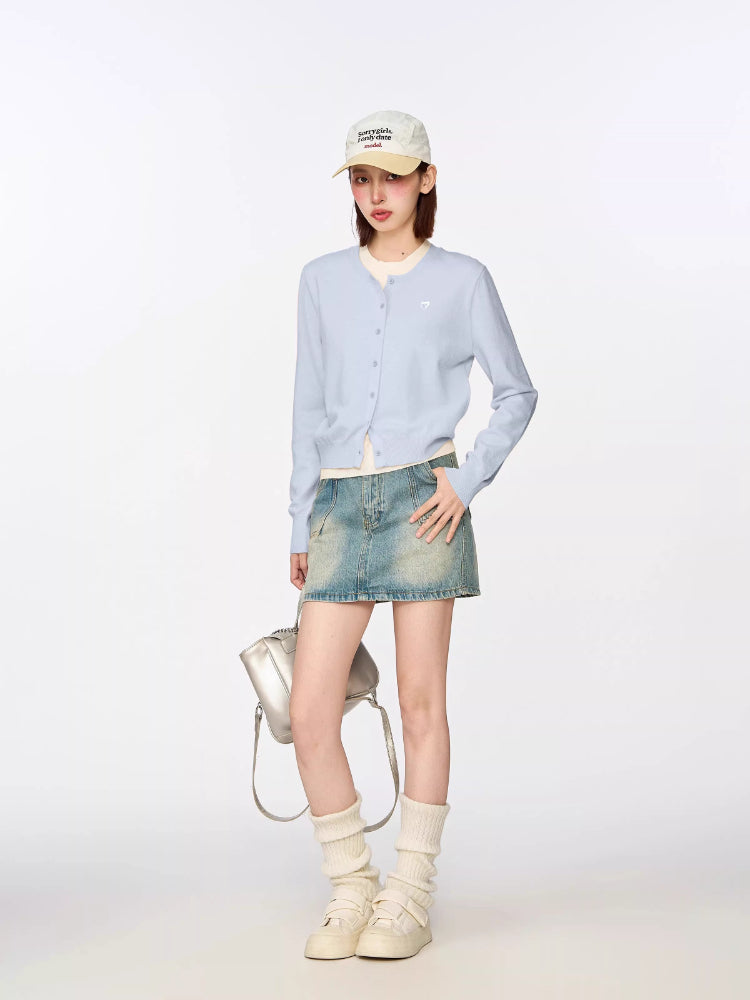 Side view of a model in a light blue cropped cardigan, white top, denim mini skirt, and accessories.
