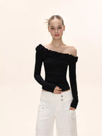 Front view of a model showcasing a black off-the-shoulder long-sleeved top with ruffled neckline and white wide-leg pants.