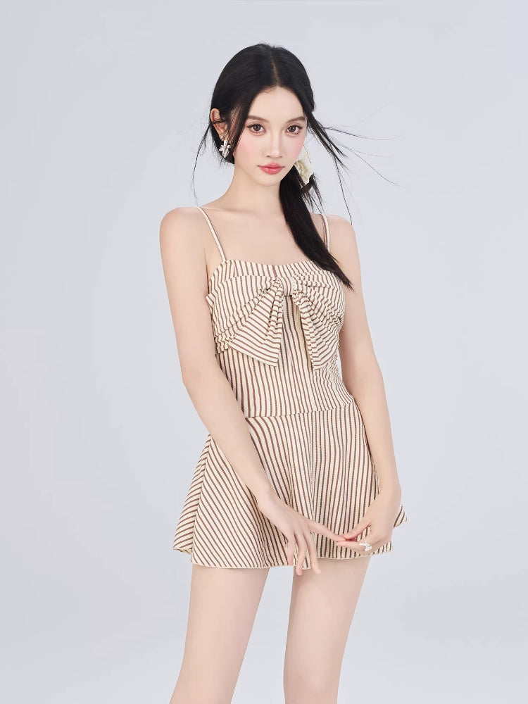 Woman posing with hands clasped in front, wearing a striped outfit with a bow detail.