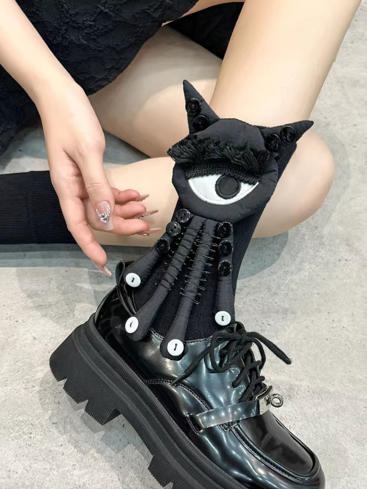 Close-up of a person wearing black socks with a black and white eye and tentacle-like attachments, paired with black platform shoes.