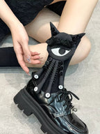 Close-up of a person wearing black socks with a black and white eye and tentacle-like attachments, paired with black platform shoes.
