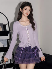 Close-up of a woman wearing a lavender ribbed knit cardigan with lace trim and bow details over a white camisole, paired with a purple tiered ruffled skirt.