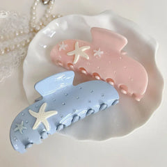 overhead view of two pastel claw clips, one pink and one light blue, with starfish and rhinestones, on a white dish
