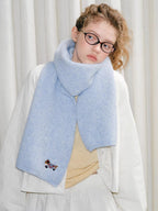 A young woman models a light blue fuzzy knit scarf featuring a small embroidered dog.