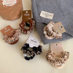 Group of scrunchies presented on a grey knit fabric, alongside other accessories