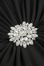 Close-up of a sparkling, multi-faceted jeweled brooch on a black ruched dress.