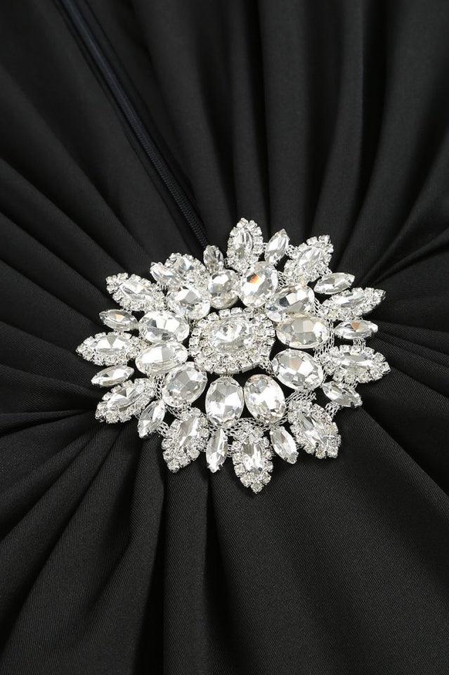 Close-up of a sparkling, multi-faceted jeweled brooch on a black ruched dress.